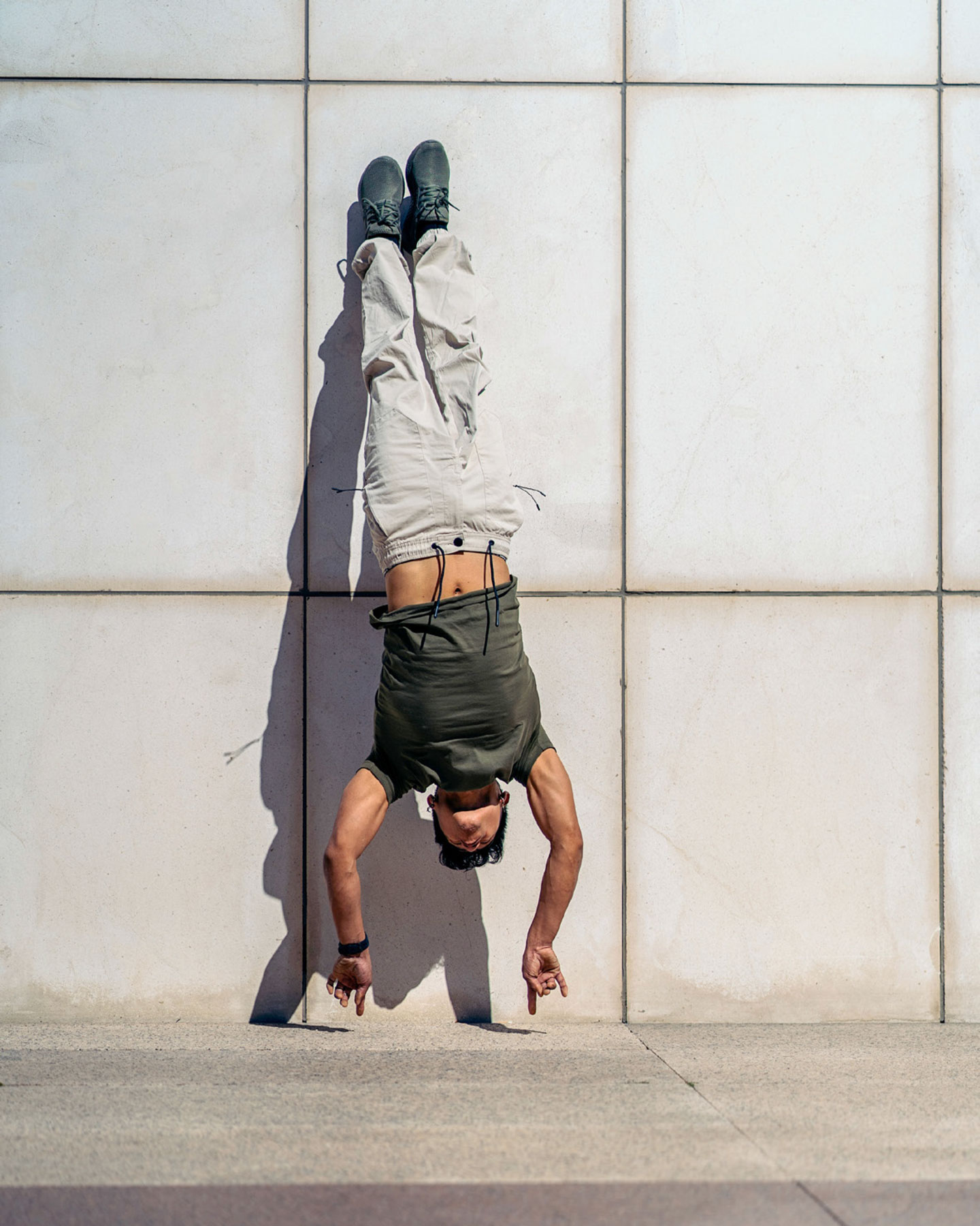 Ein junger Mann scheint auf den ersten Blick einen Handstand zu machen, doch seine Hände berühren den Boden nicht: Hängt er an der Wand?