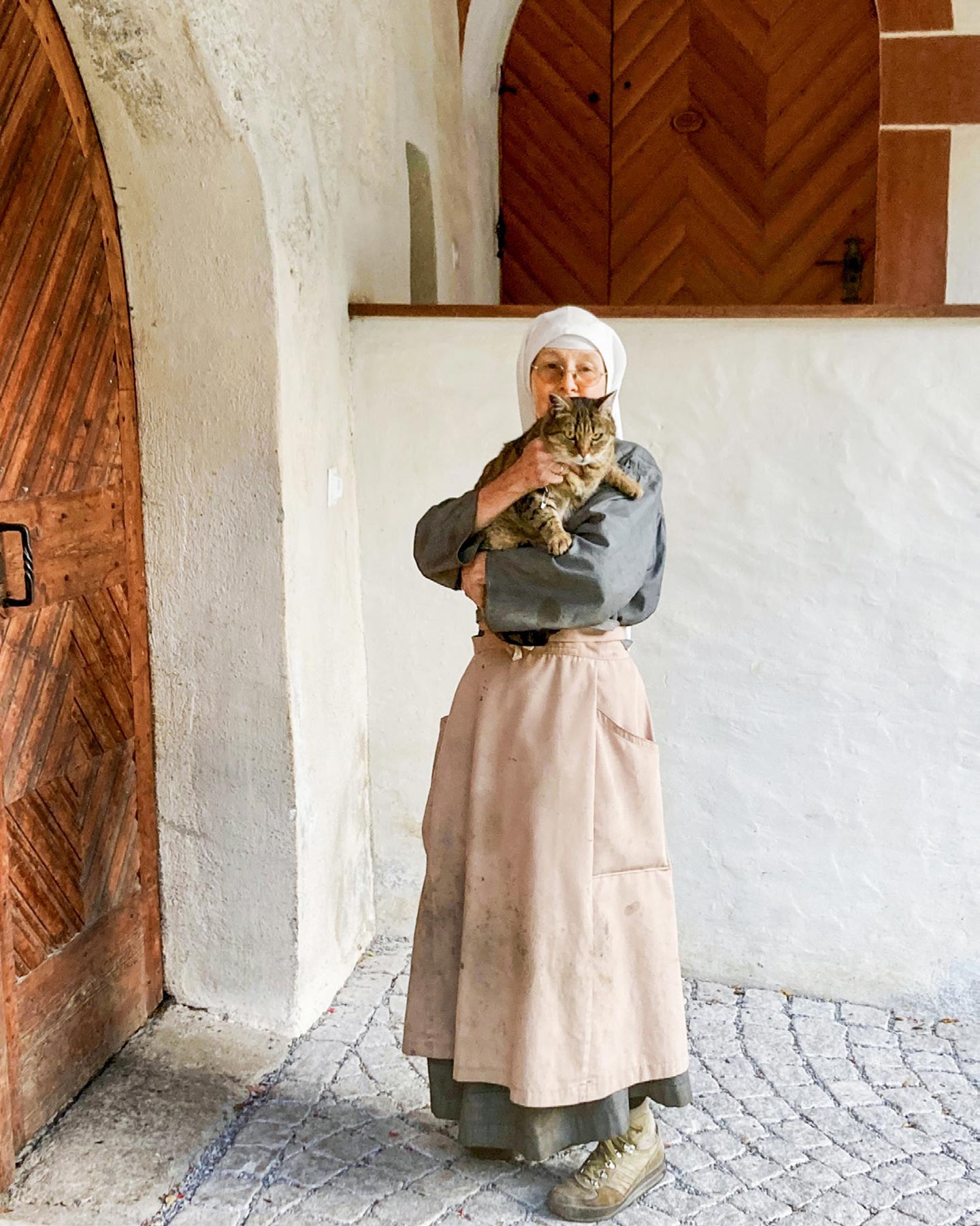 Eine Nonne mit einer Katze auf dem Arm in den Gemäuern ihres Klosters