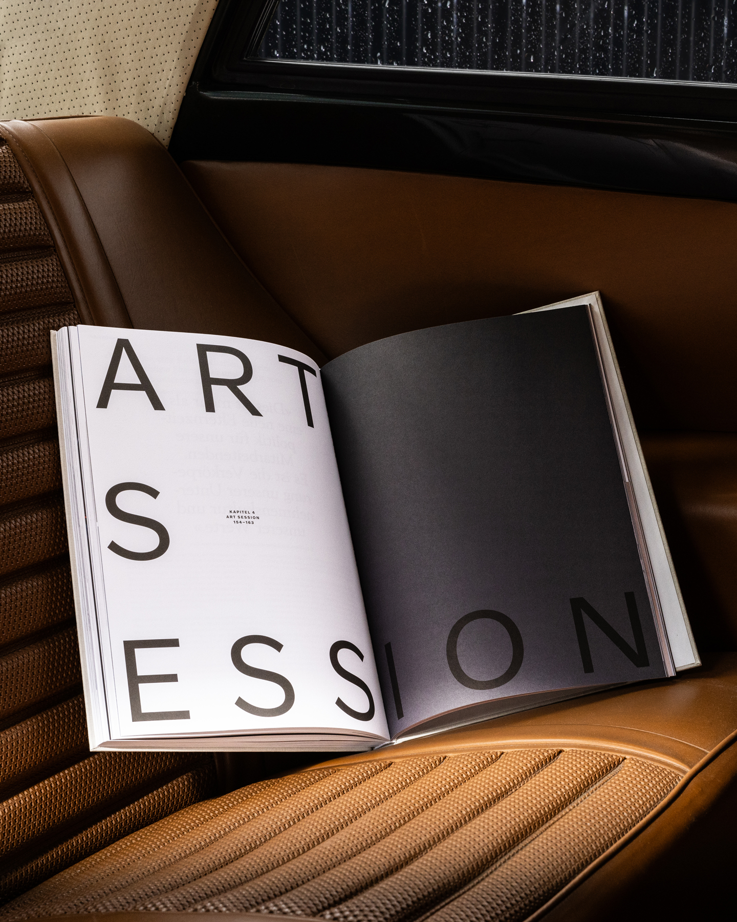 Das Volvo-Buch liegt aufgeschlagen auf dem Ledersitz eines Volvos und zeigt die grau-weisse Einstiegsdoppelseite des Kapitels «Art Session».