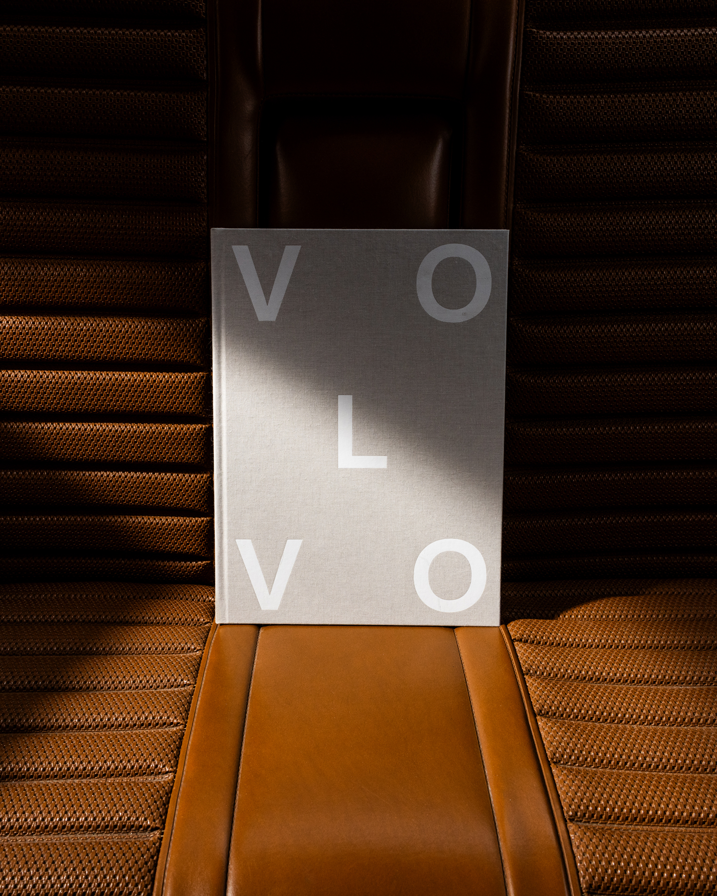 Das Volvo-Buch mit seinem schlichten grauen Einband steht auf dem Ledersitz eines Volvos.