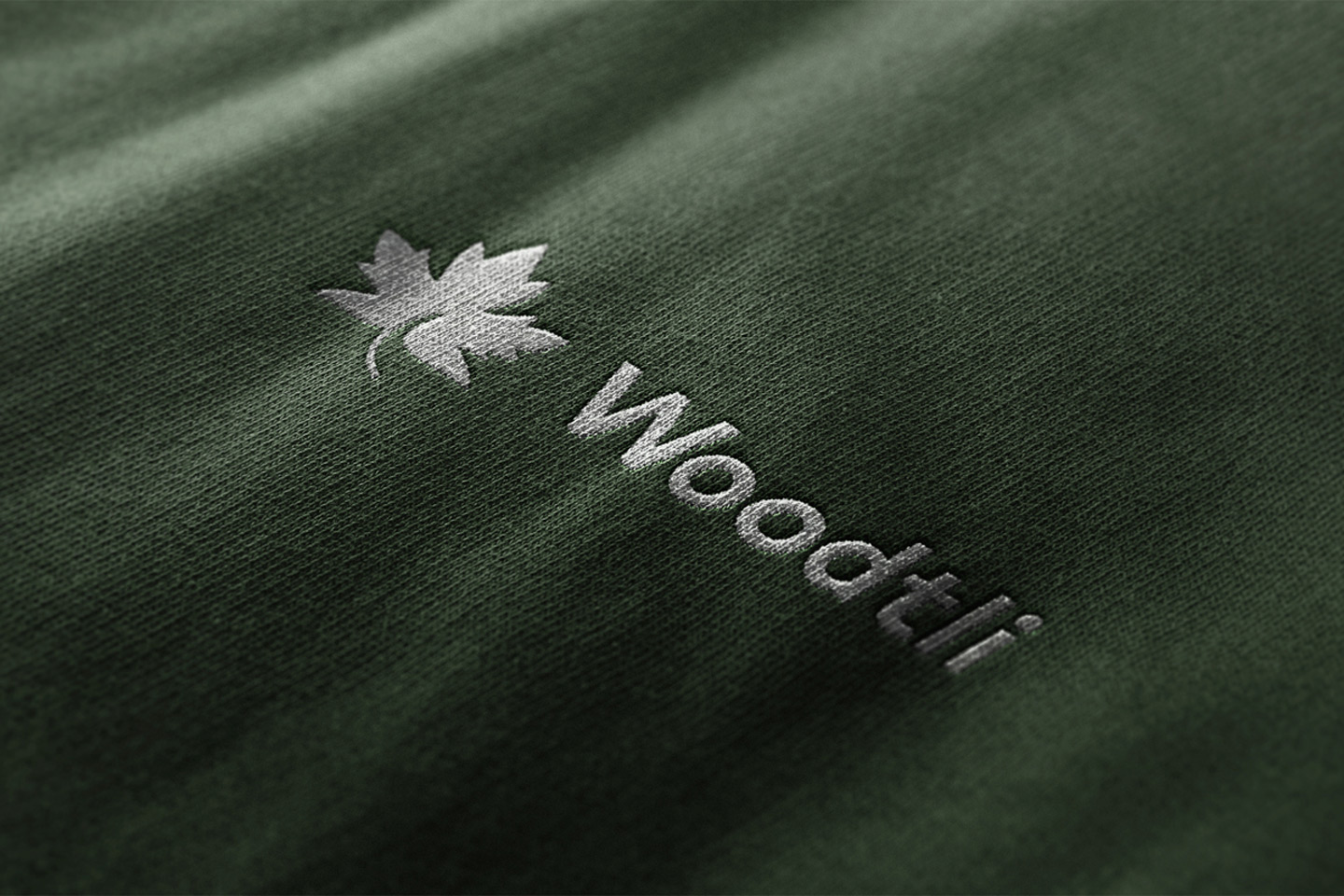 Logo Mockup Collection by Asylab Das neue Woodtli-Logo enthält ein Ahornblatt. Hier erscheint es in Weiss auf blassgrünem Stoff.