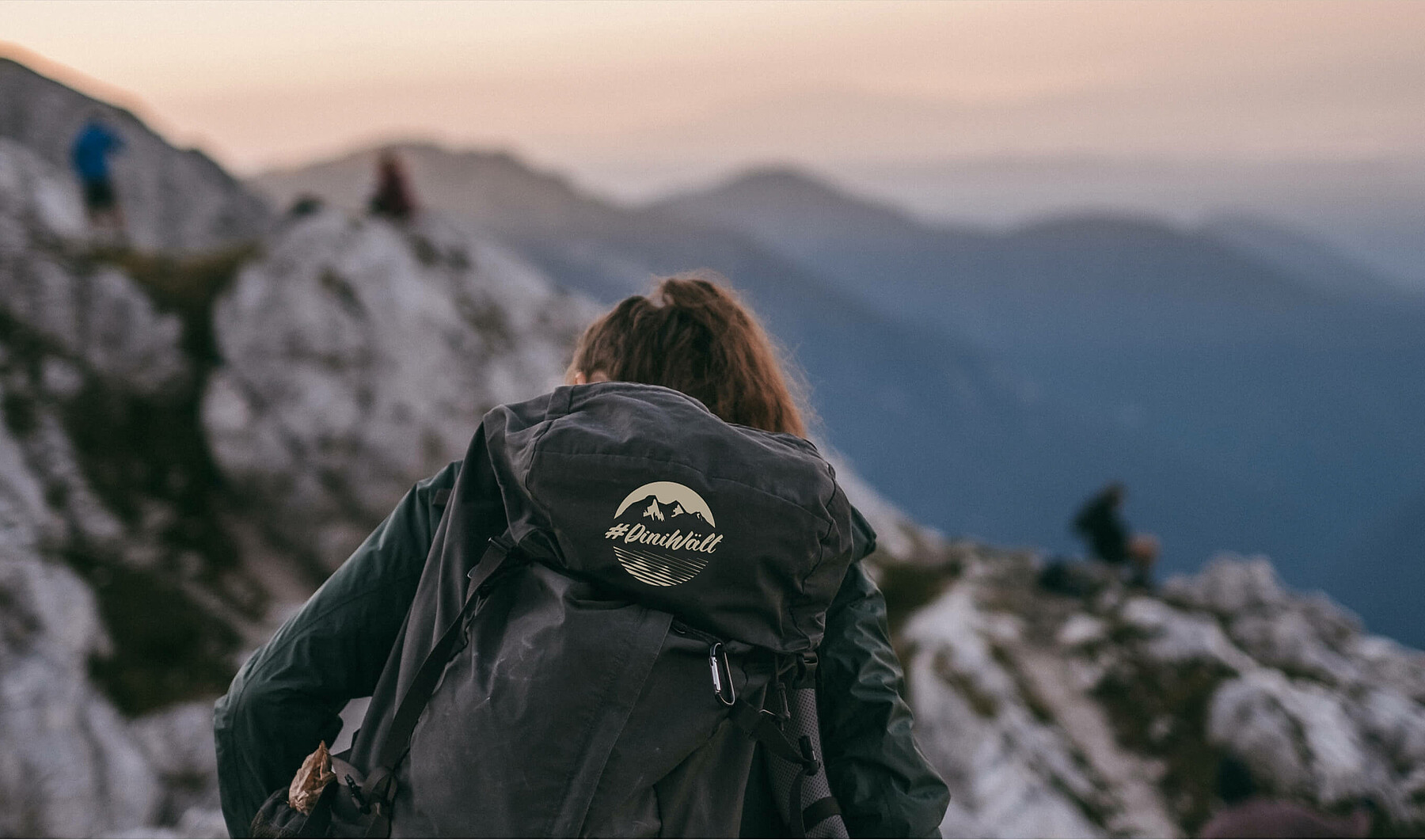Eine Frau in den Bergen trägt einen Rucksack mit dem Label #DiniWält der Jungfrau-Region.