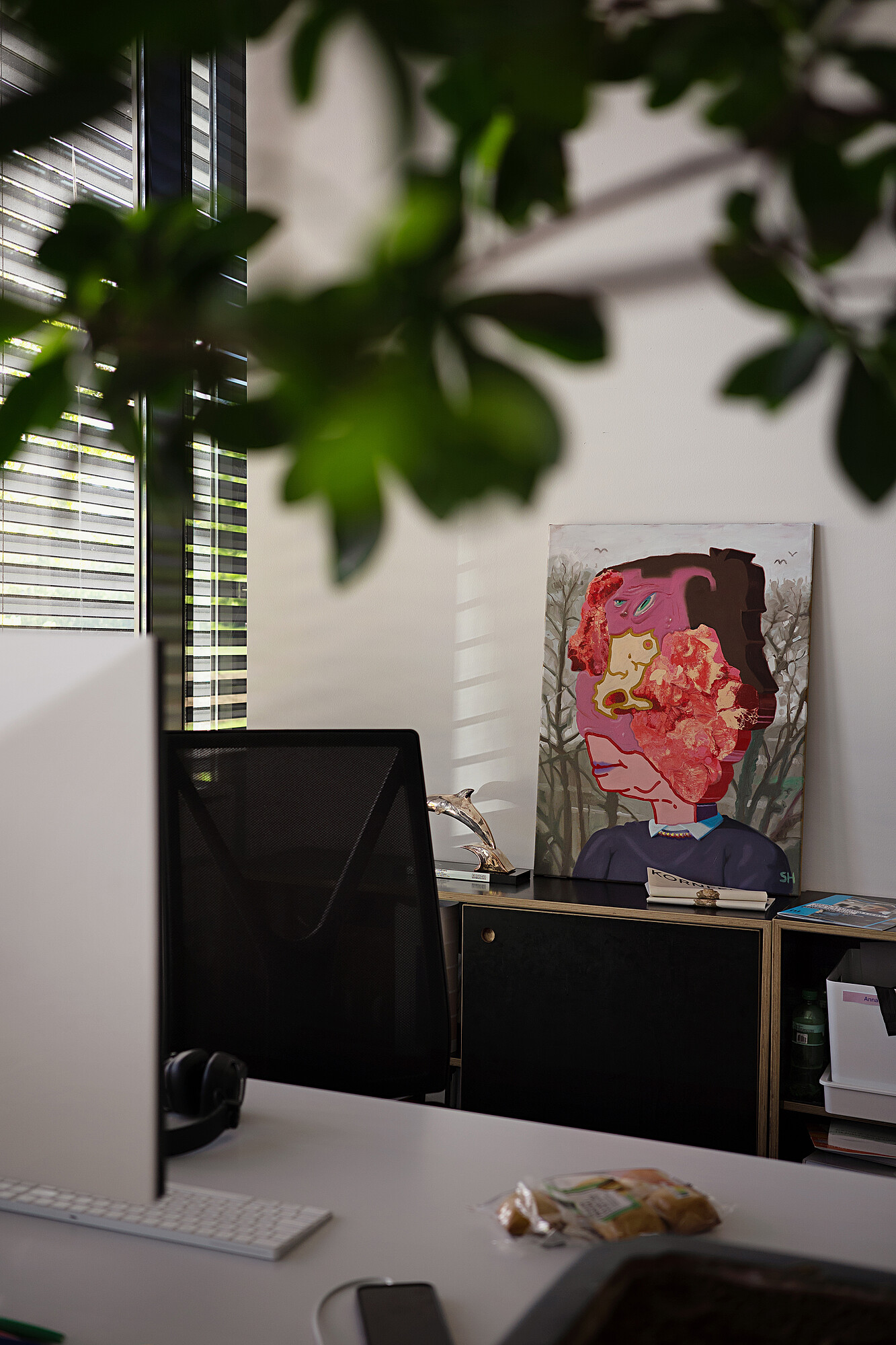 Un portrait coloré, peint de manière abstraite, est adossé au mur d’un bureau.