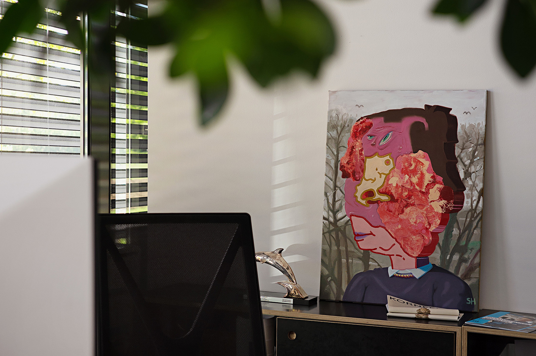 Ein buntes, abstrakt gemaltes Porträt lehnt an einer Bürowand.