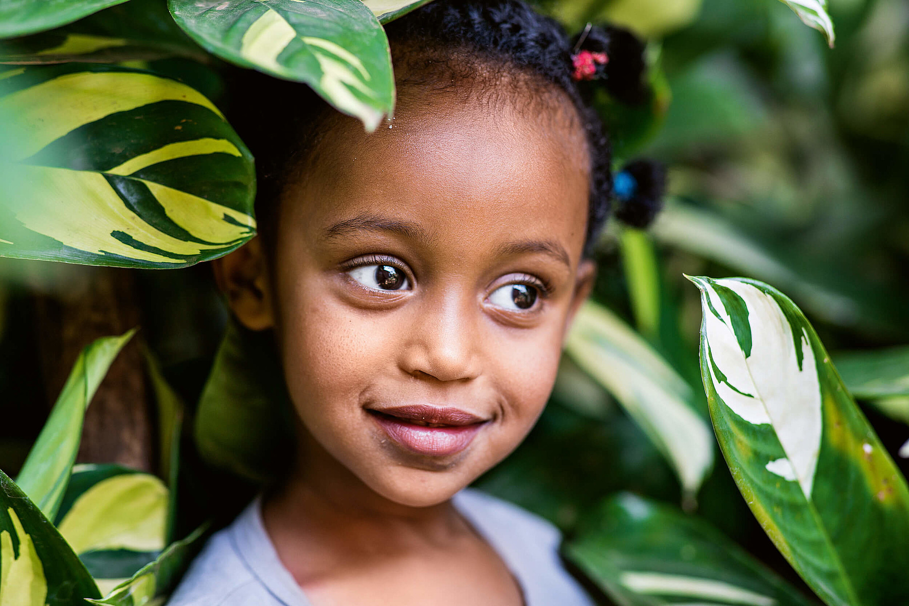 Ein kleines afrikanisches Mädchen steht inmitten einer grünen Pflanze und lächelt.