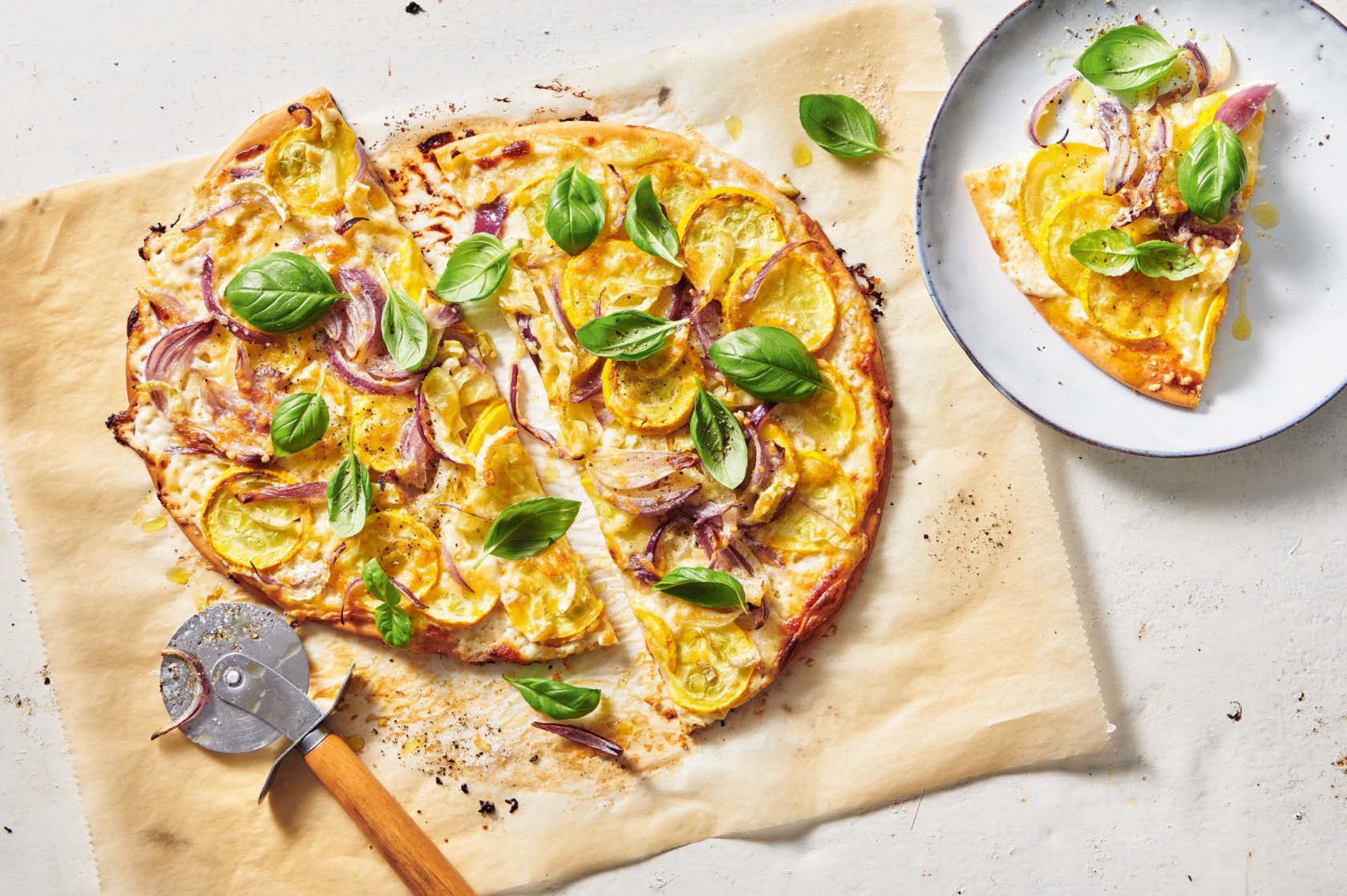 [Translate to Französisch:] Eine knusprige Pizza mit gelben Zucchetti und roten Zwiebeln, bestreut mit frischem Basilikum