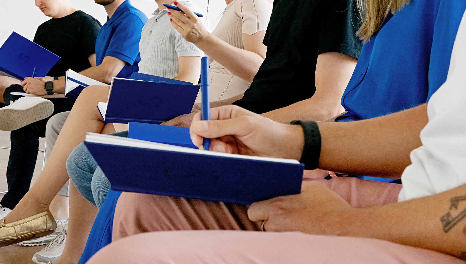 Nahaufnahme der Hände und des Schosses einer Zuhörerin bei einem Vortrag. Sie macht sich Notizen.