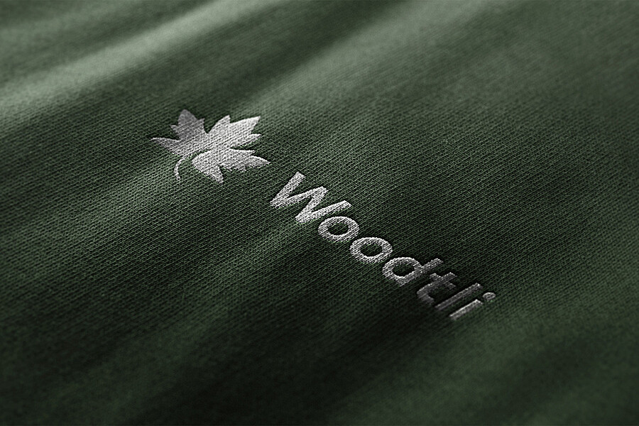 Das neue Woodtli-Logo enthält ein Ahornblatt. Hier erscheint es in Weiss auf blassgrünem Stoff.