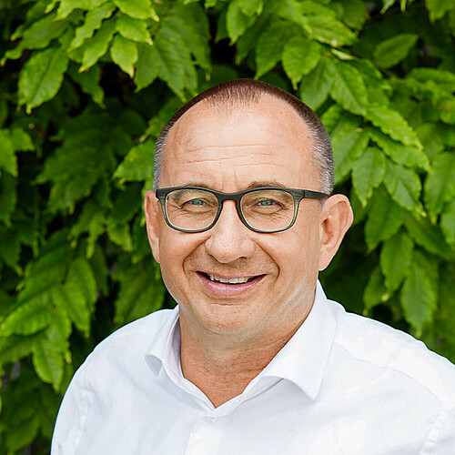 Inhaber Daniel Witschi lacht vor saftig grünen Buchenblättern in die Kamera.