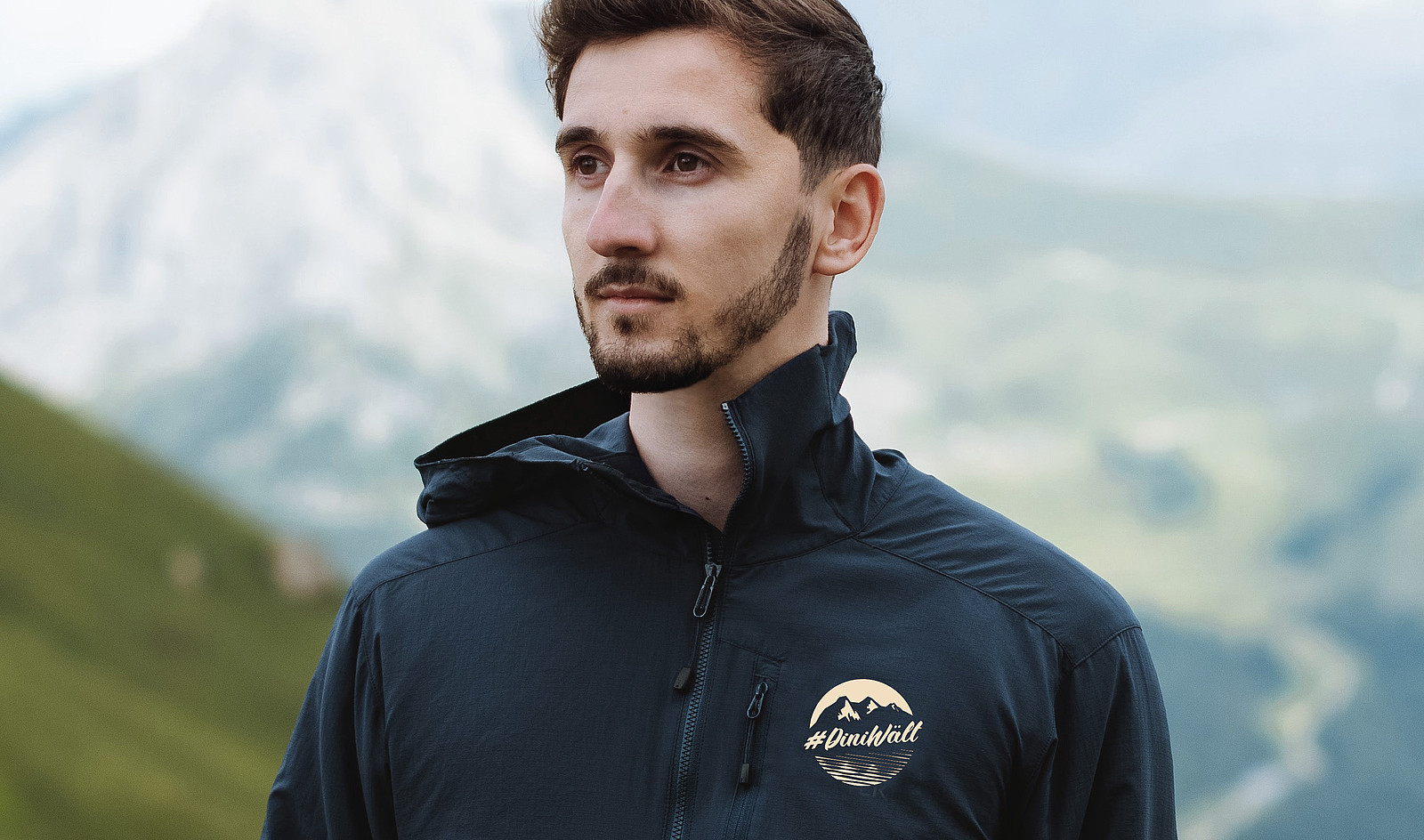 Ein Mann in den Bergen trägt eine sportliche Jacke mit dem Label #DiniWält der Jungfrau-Region.