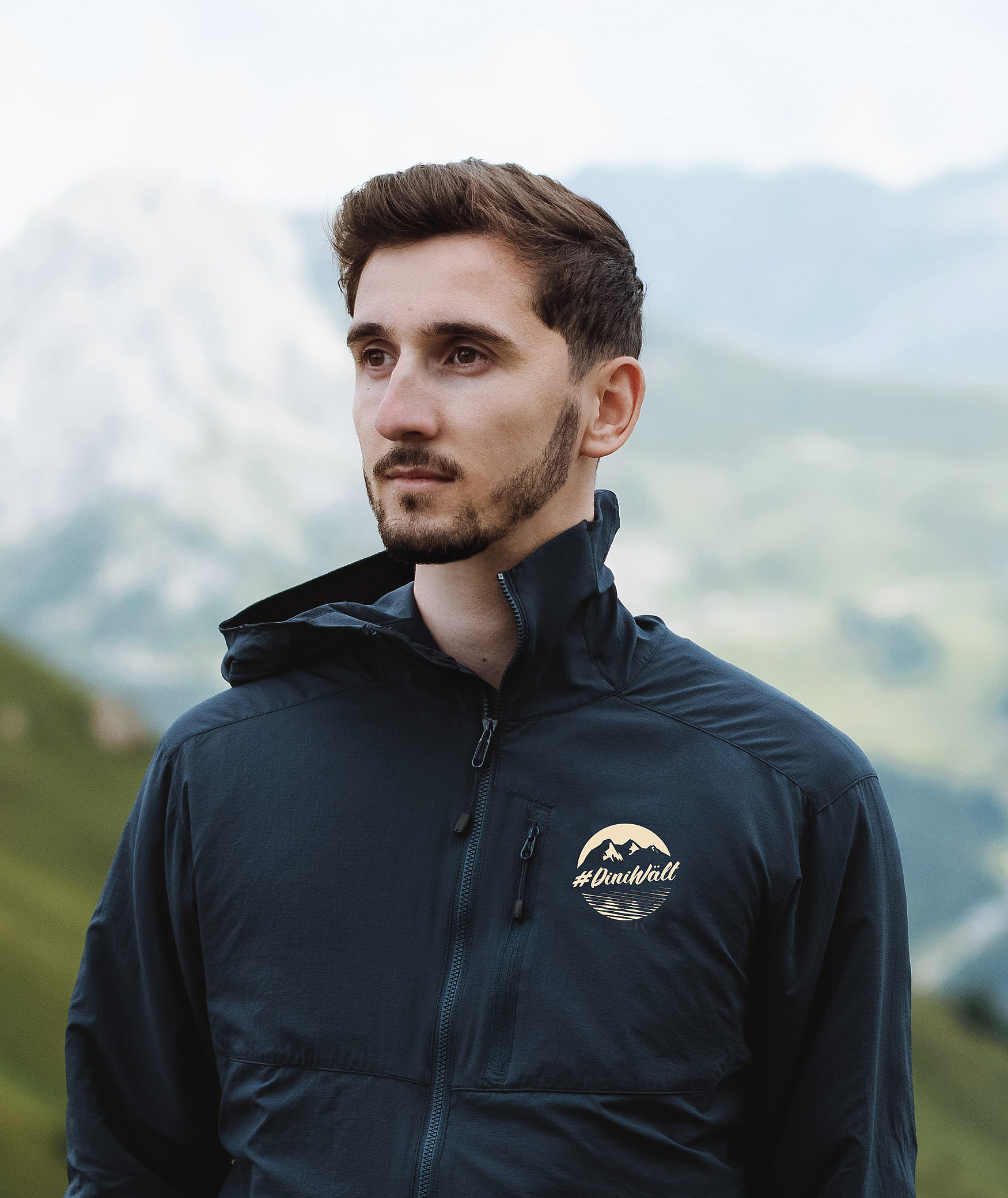 Ein Mann in den Bergen trägt eine sportliche Jacke mit dem Label #DiniWält der Jungfrau-Region.