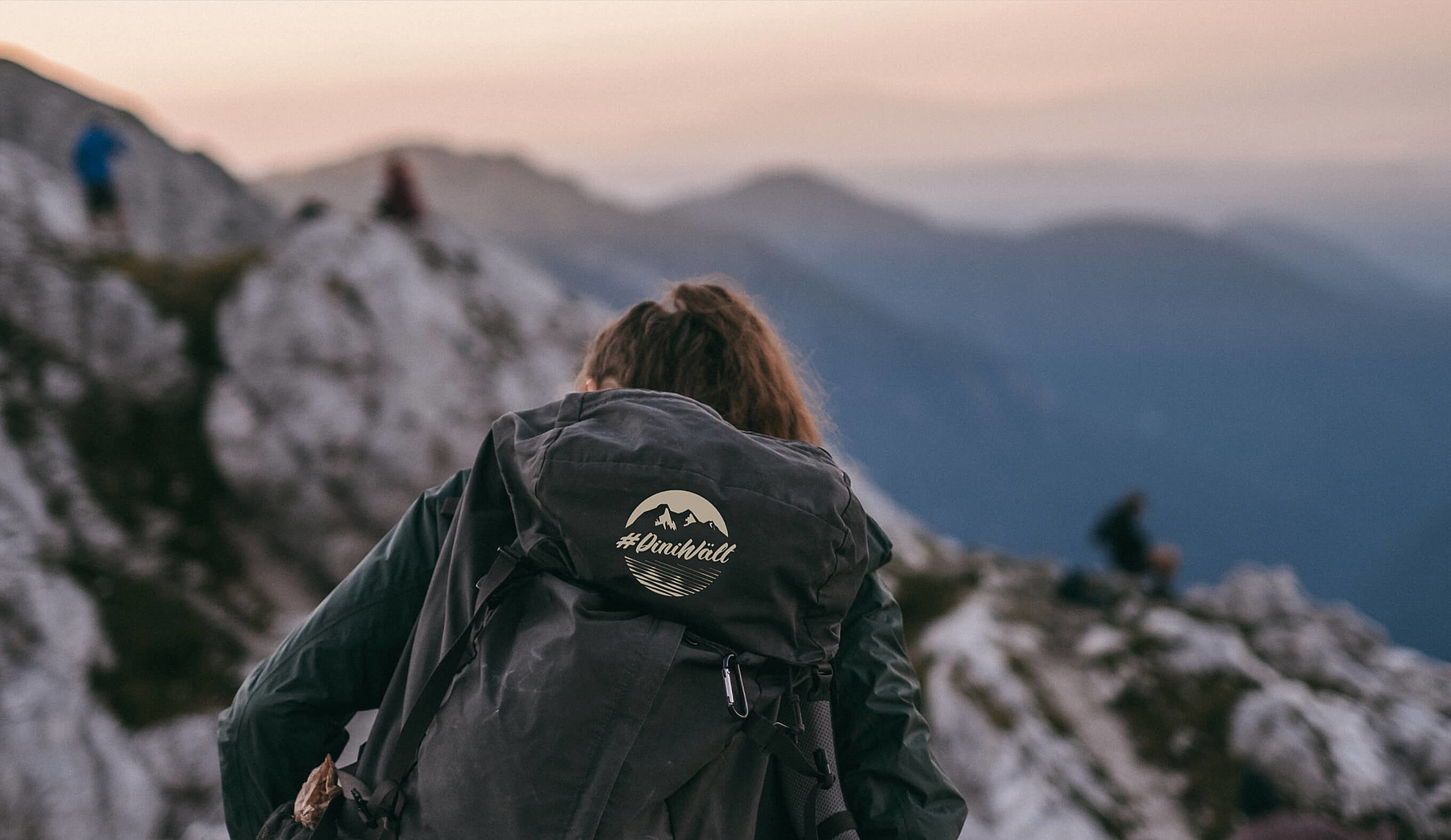 Eine Frau in den Bergen trägt einen Rucksack mit dem Label #DiniWält der Jungfrau-Region.