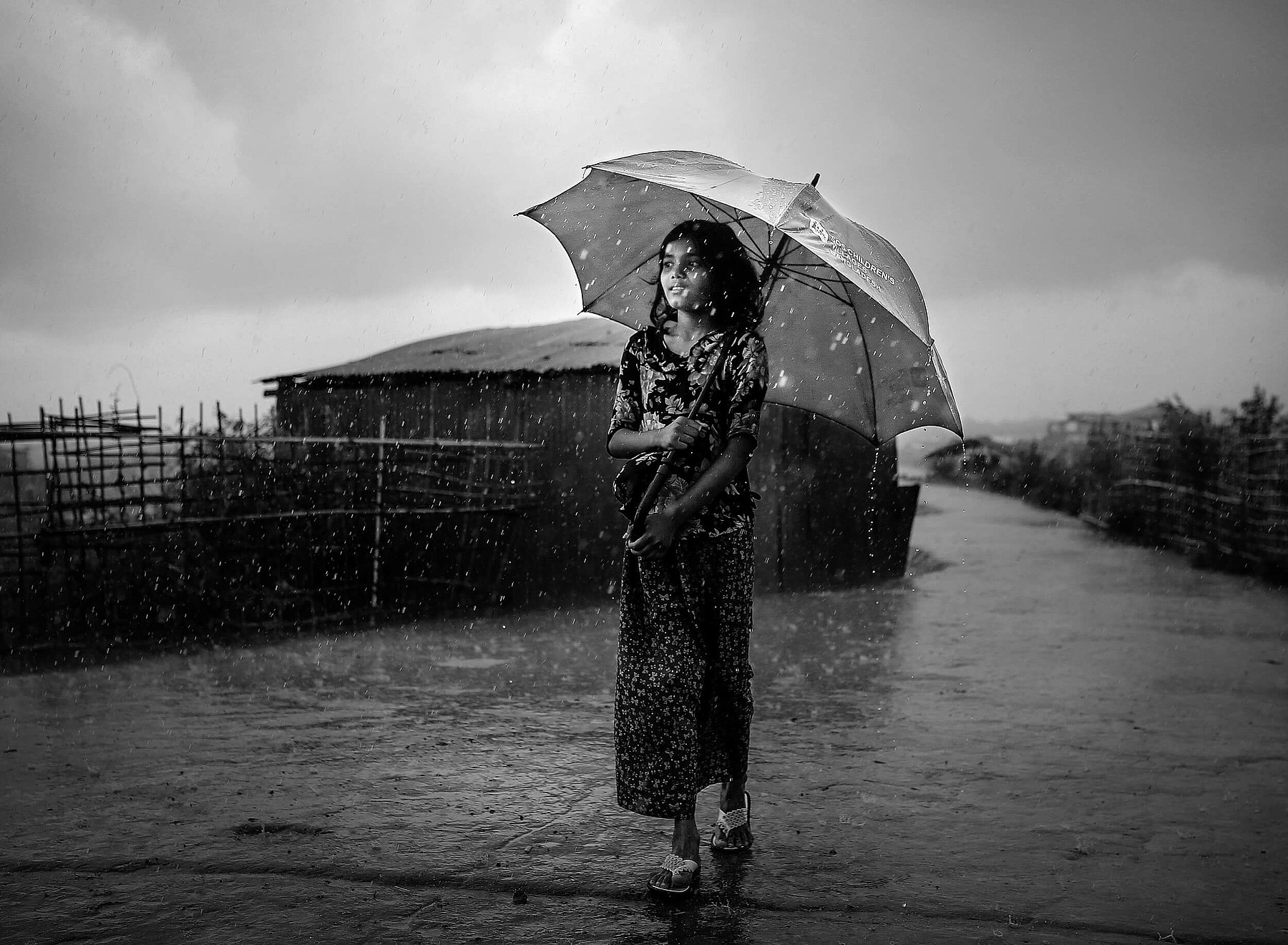 Ein Schwarz-Weiss-Foto eines Mädchens, das mit Schirm und Flipflops durch den Monsunregen geht.