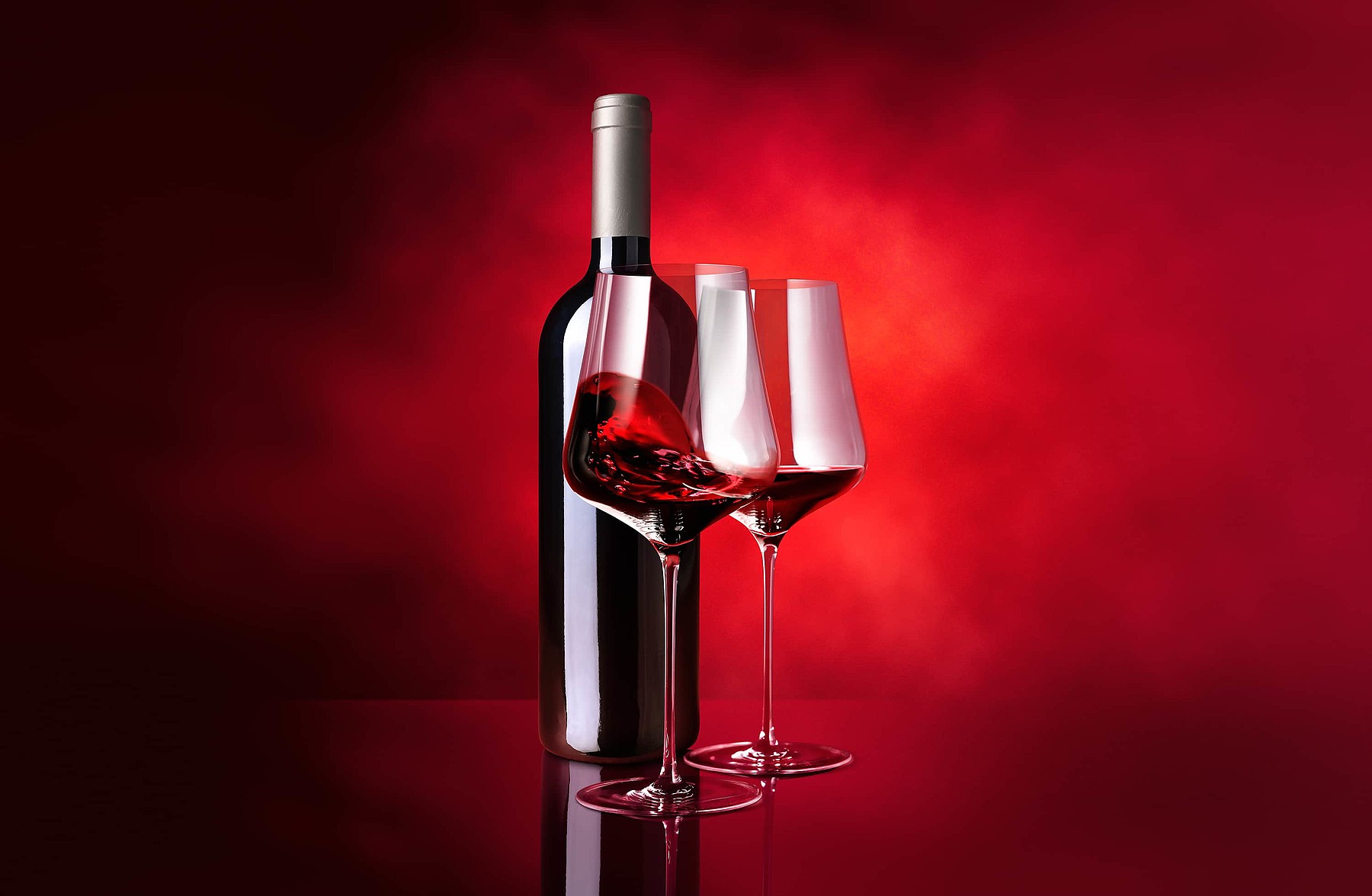 Zwei Gläser Rotwein und eine Weinflasche vor hellrotem Hintergrund