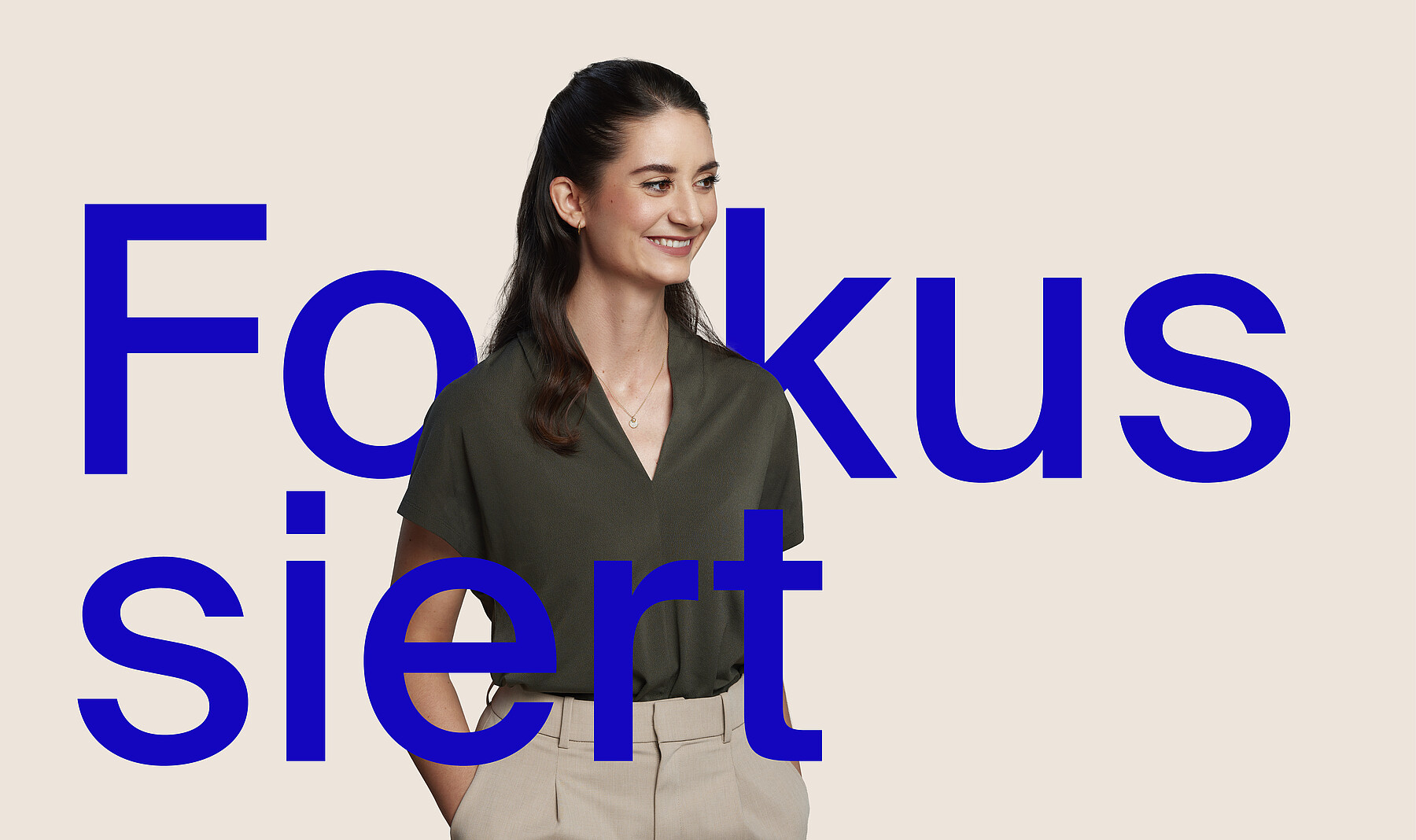 Junge Frau mit freundlichem, offenem Lächeln, langen dunklen Haaren und olivfarbener Bluse. Bei ihr steht in grossen blauen Buchstaben Fokussiert.