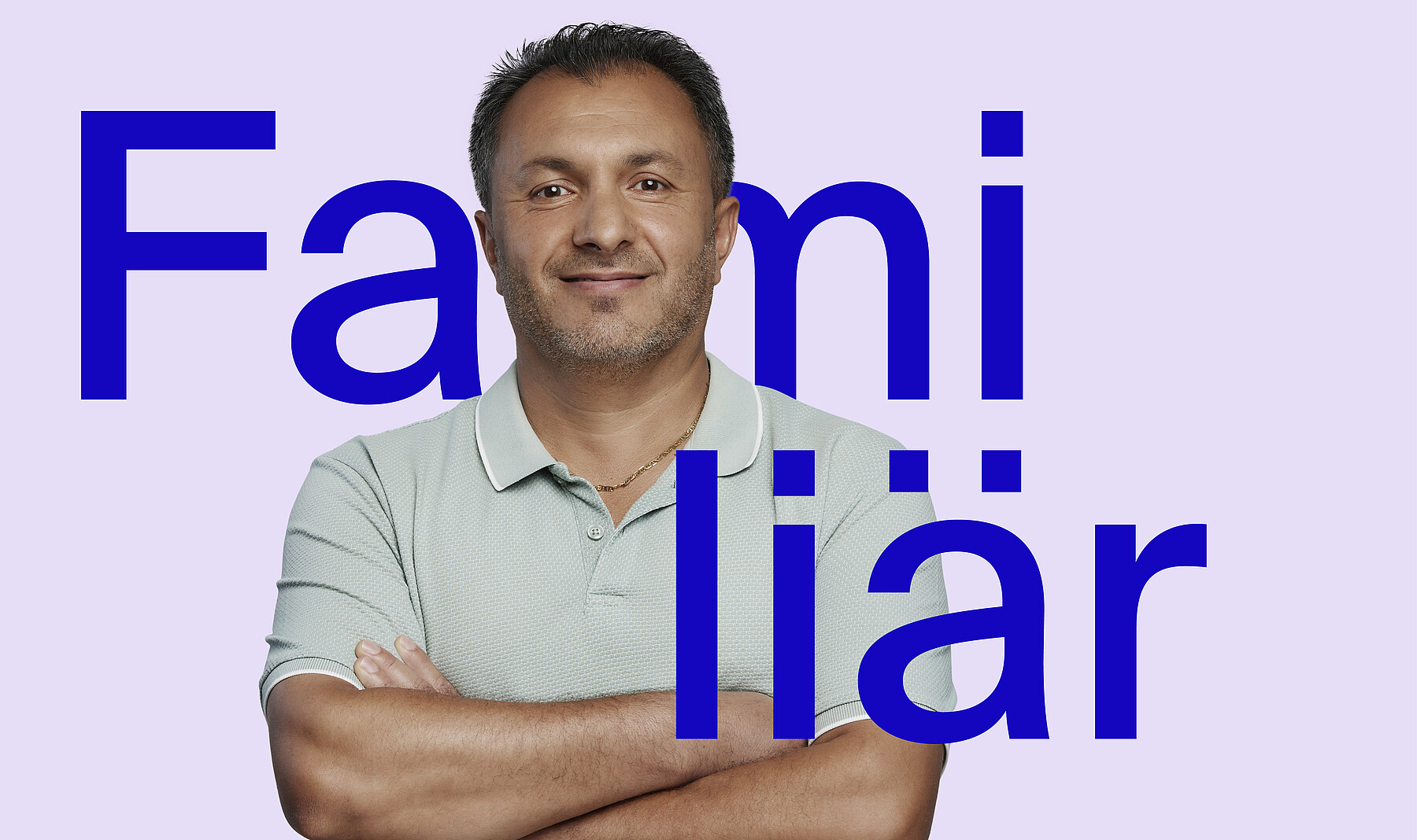 Mann mittleren Alters mit freundlichem Lächeln, dunklen Haaren und hellem Poloshirt, die Arme verschränkt. Bei ihm steht in grossen blauen Buchstaben das Wort Familiär.