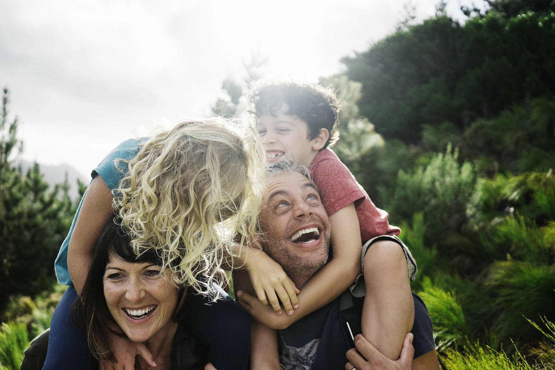 Eine fröhliche Familie beim Wandern: Die Kinder sitzen den Eltern auf den Schultern.