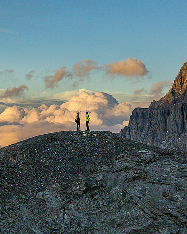 Zwei einsame Wanderer stehen auf einem Gipfel und geniessen die schöne Stimmung.