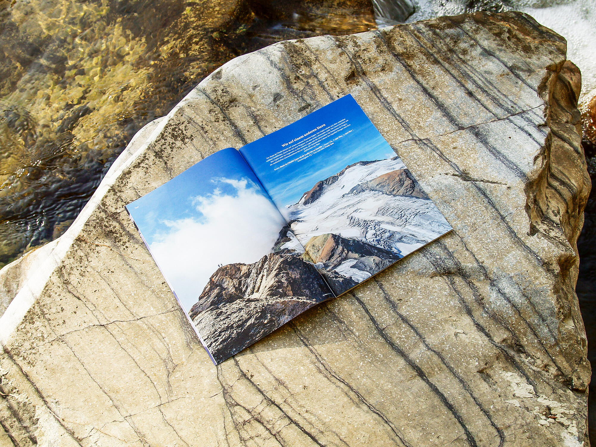 Eine aufgeschlagene Ausgabe der SAC-Zeitschrift «Die Alpen» auf einem Felsbrocken im Grünen: Sie zeigt ein doppelseitiges Schwarz-Weiss-Foto einer Felslandschaft.