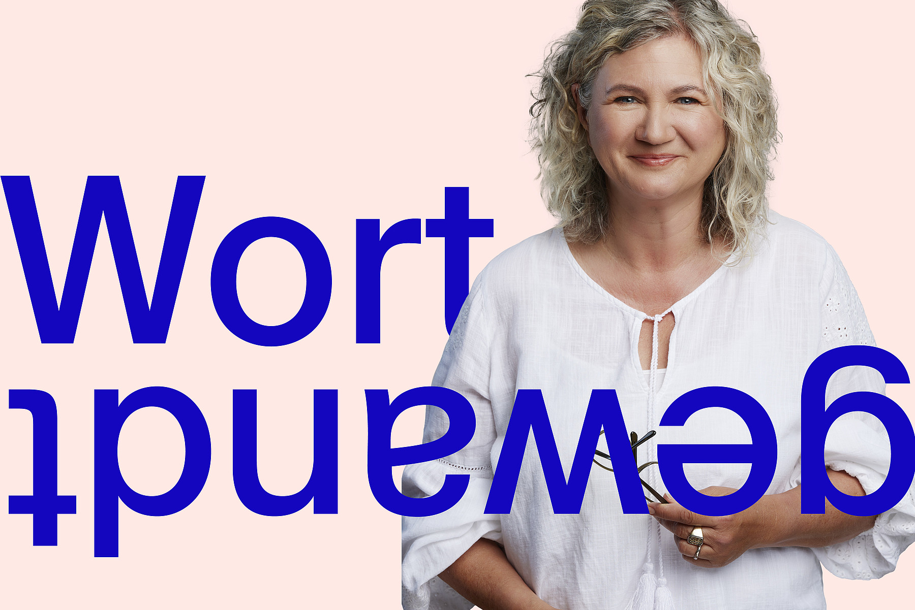 Frau mittleren Alters mit warmem Lächeln, blonden Locken, weisser Bluse und Lesebrille in der Hand. Bei ihr steht in grossen blauen Buchstaben das Wort Wortgewandt, die zweite Hälfte davon auf dem Kopf.