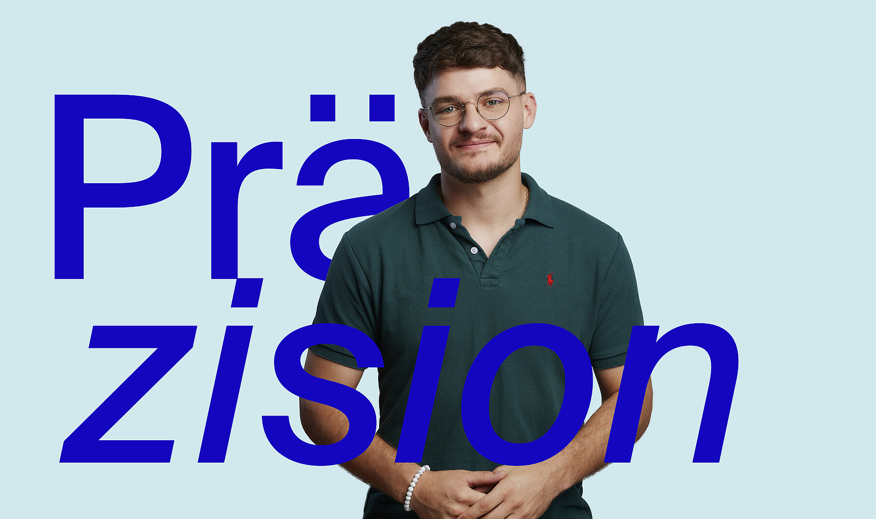 Junger Mann mit warmem Lächeln, dunklen Haaren und petrolfarbenem Poloshirt. Bei ihm steht in grossen blauen Buchstaben das Wort Präzision.
