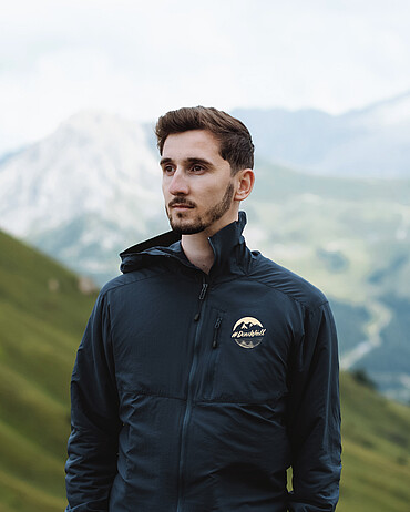Ein Mann in den Bergen trägt eine sportliche Jacke mit dem Label #DiniWält der Jungfrau-Region.