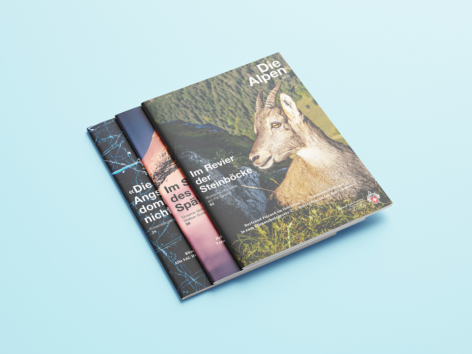 Mockups Design Drei aufeinanderliegende Exemplare des Magazins «Die Alpen»: Das Cover der obenauf liegenden Ausgabe 9/2021 zeigt einen Bergsteiger auf einem Gipfel bei Sonnenaufgang.