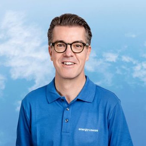 Ein Mann mittleren Alters mit Brille und sympathischem offenem Lachen in einem blauen Poloshirt